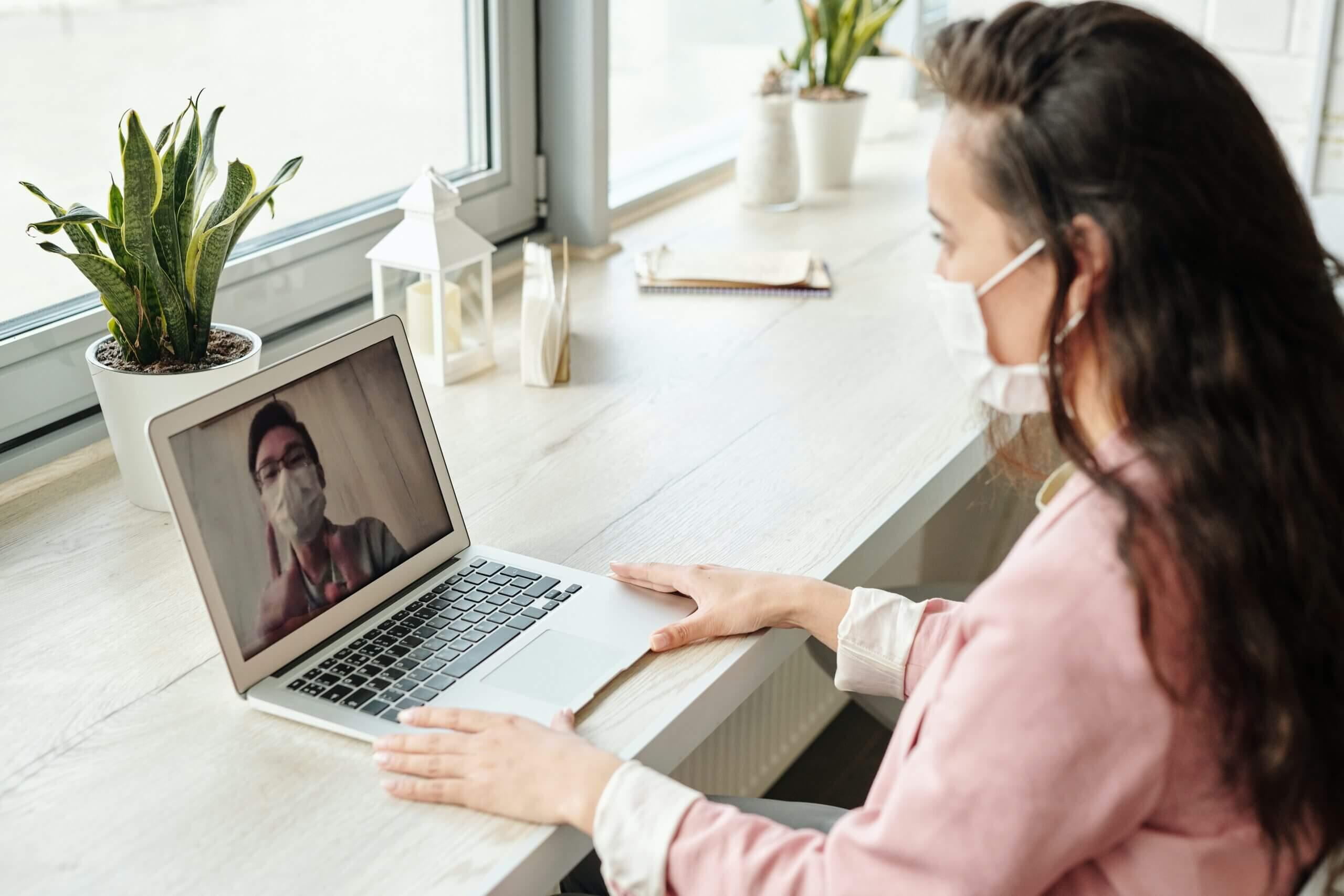 Girl with face mask talking to a guy using her laptop during quarantine
