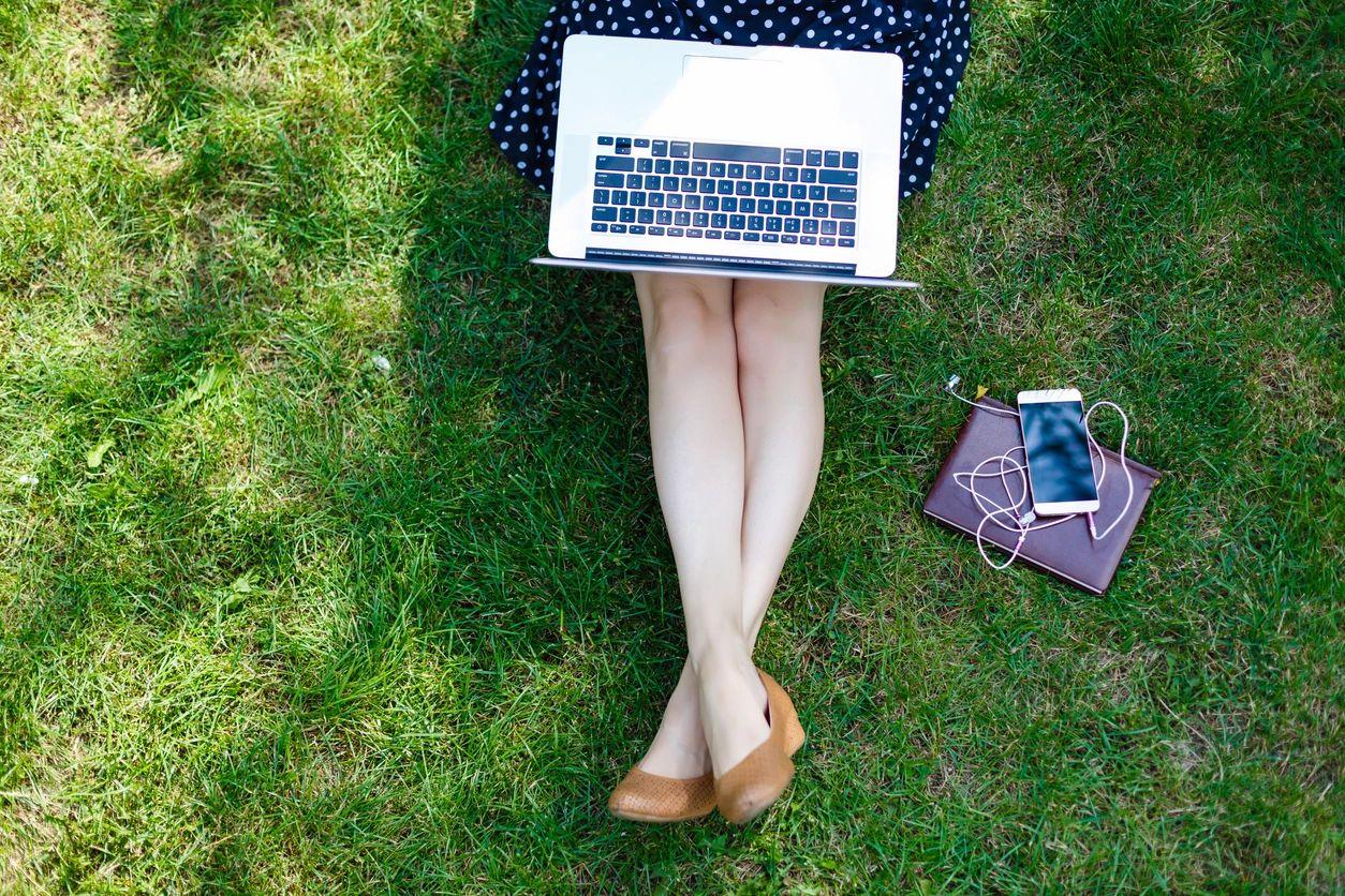 Single lady in polka dot dress sitting on the grass with a laptop on her lap