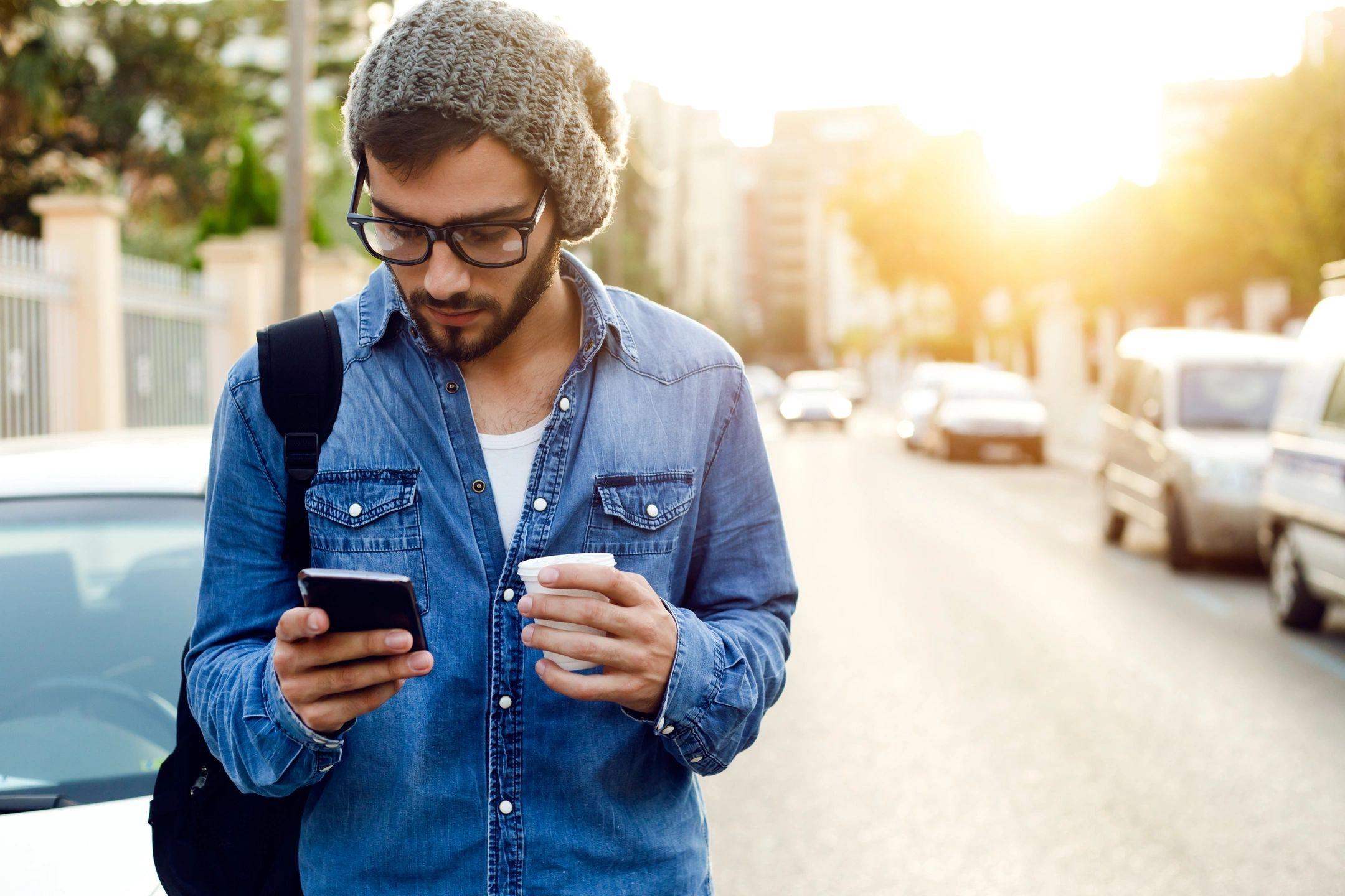 Man holding coffee while searching for single girls using his smartphone